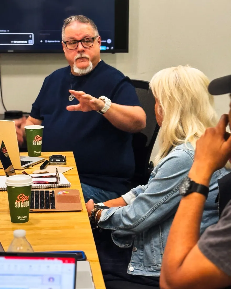 Harrison Painter leaning in at the table, explaining a step directly to one participant while she works on her laptop.
