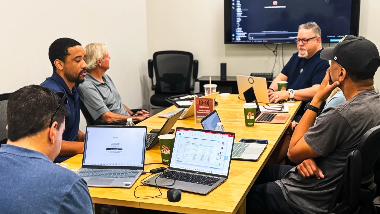 Participants at a LaunchReady AI workshop working on their own laptops around one table while Harrison Painter works alongside them.